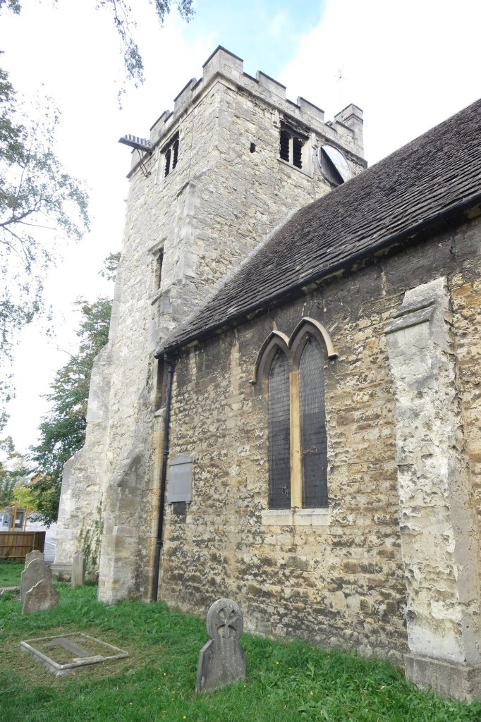 Side view of a stone church with a tall tower and a graveyard in the foreground.